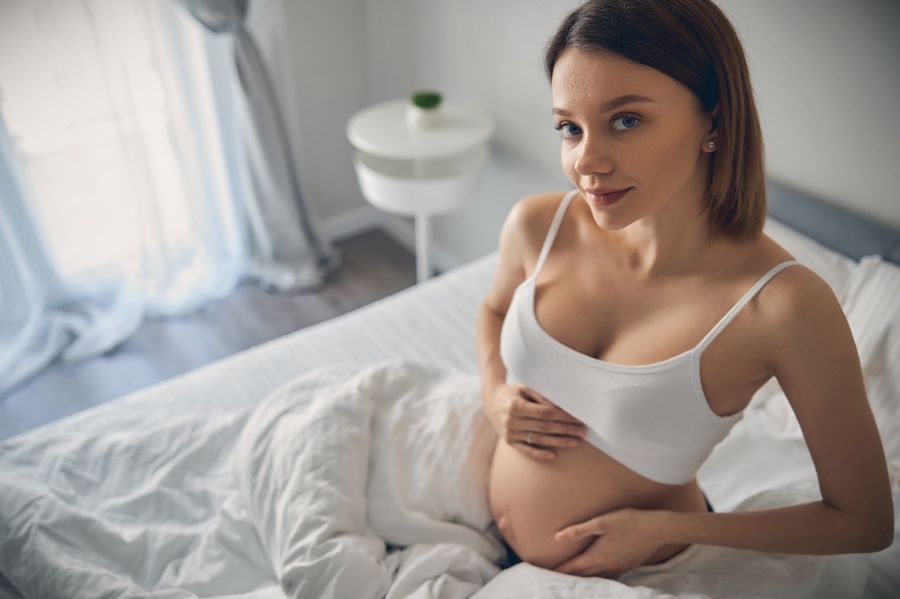 Mujer embarazada en la cama con sujetador premamá